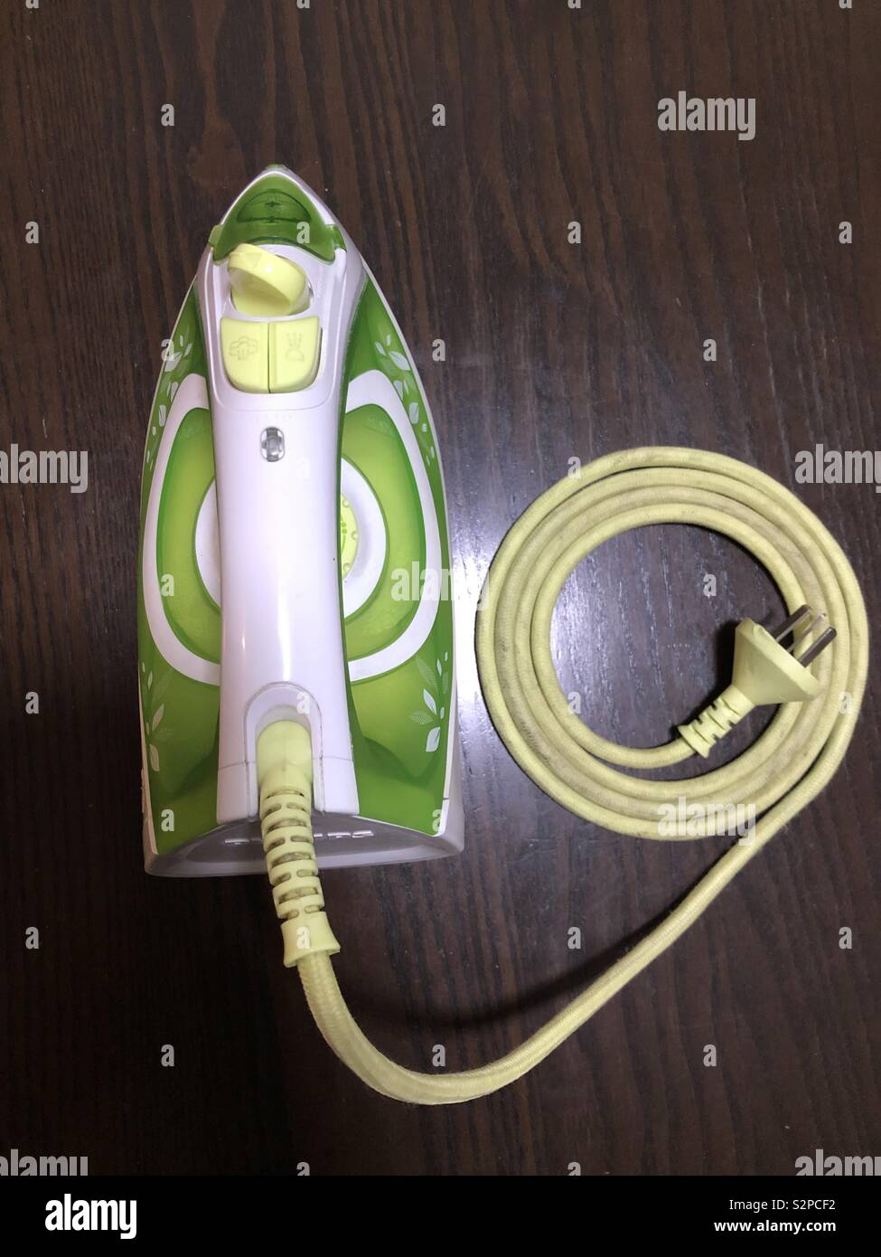 Green and white iron flat on the surface with coiled cable beside it and Asian plug in the middle of the coil. Stock Photo