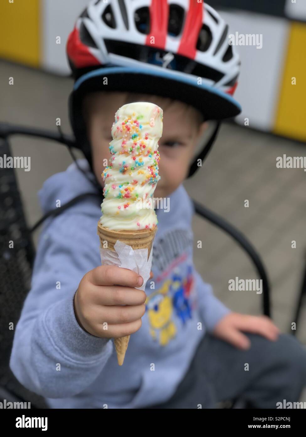 Toddler eating ice cream with sprinkles outside with a bike helmet on Stock Photo
