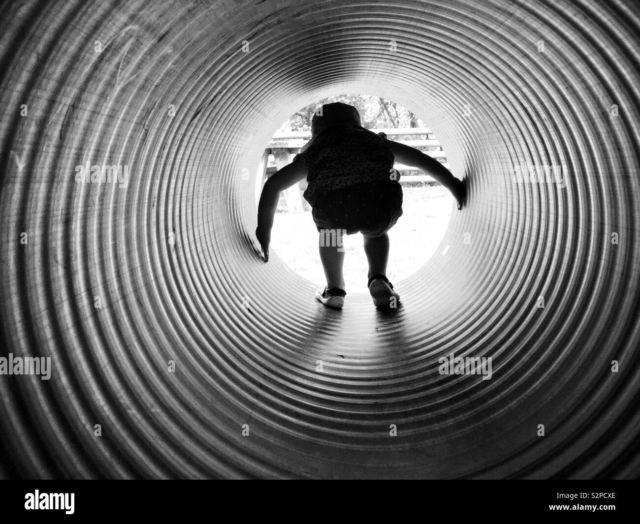 Black and white silhouette of child crawling through a tube or pipe at an adventure playground Stock Photo