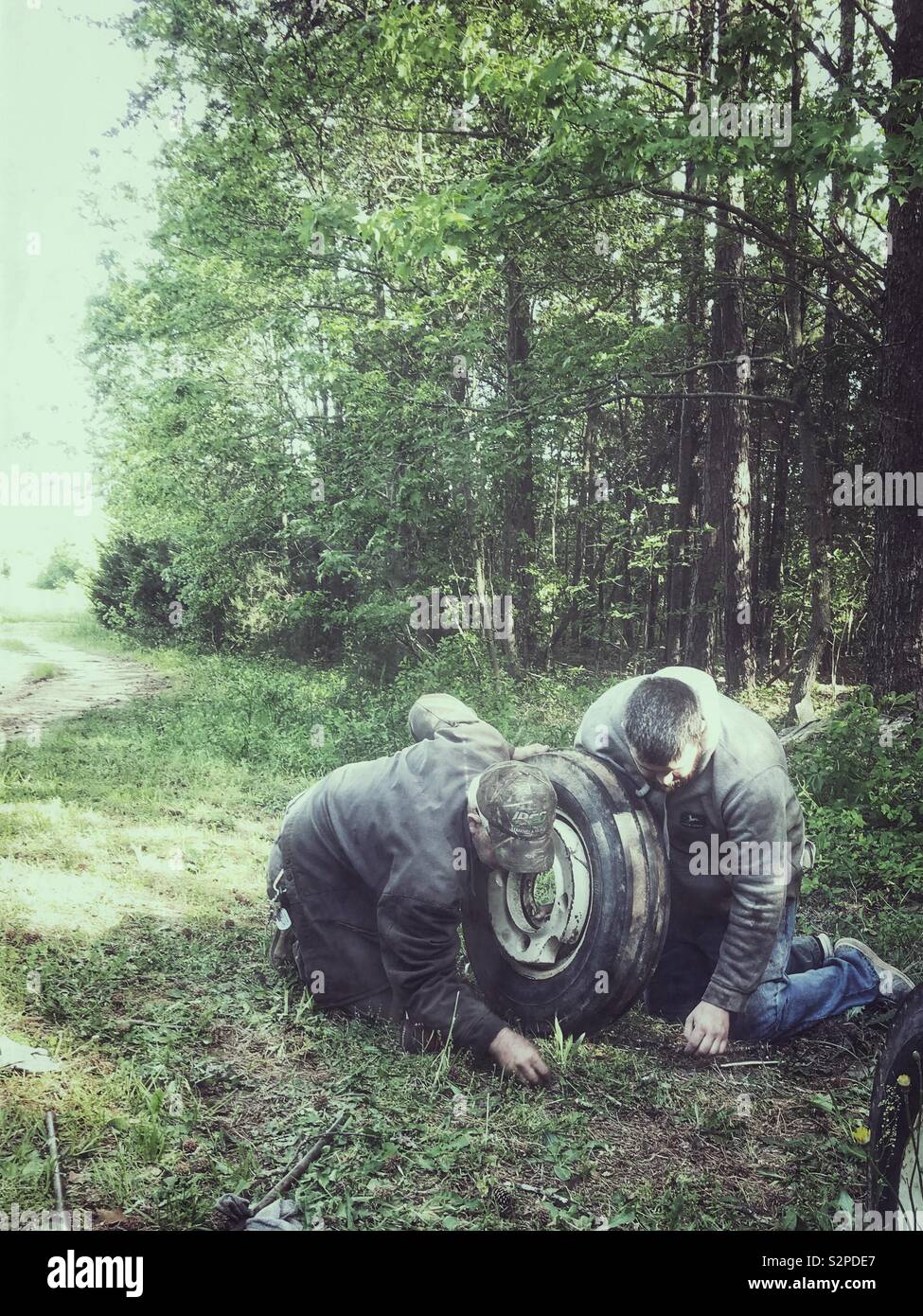 Father and grown son working together replacing tractor tire on the farm - Smartphone Captured Stock Image