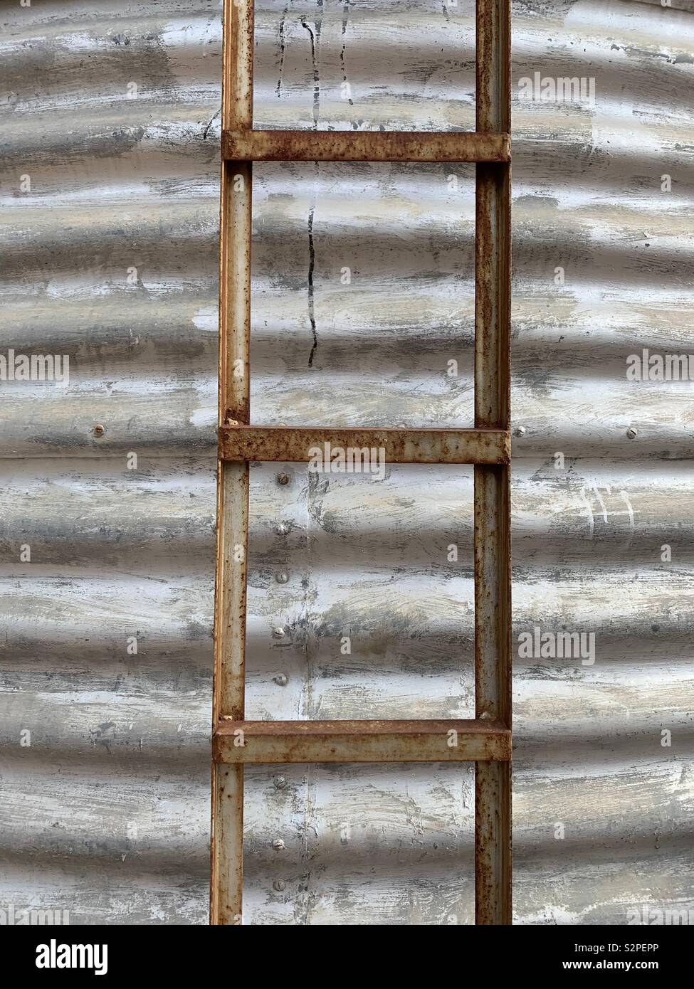 A rusty ladder stands against an old grey silver water tank on a farm in northwest New South Wales, Australia - Smartphone Captured Stock Image