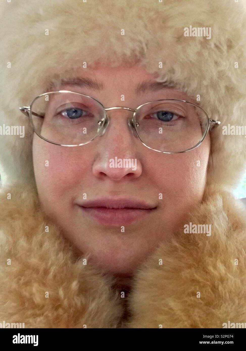 Face of Caucasian woman with blue eyes and gold rimmed glasses wearing cruelty free no-kill alpaca fur hat and scarf - Smartphone Captured Stock Image