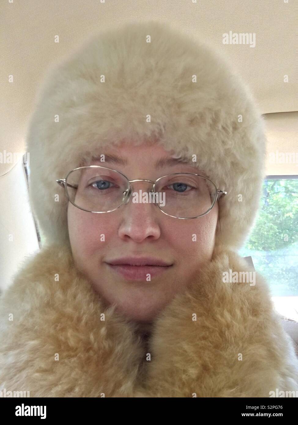 Caucasian woman with blue eyes and gold rimmed glasses inside car wearing cruelty free no-kill alpaca fur hat and scarf - Smartphone Captured Stock Image