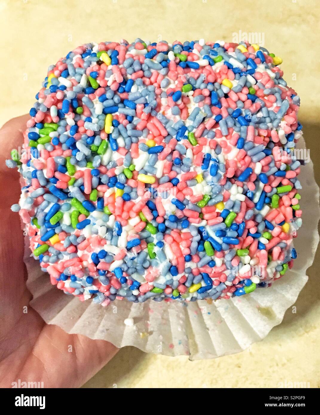 Hand holding Jimmie Cake with pink yellow green and dark and light blue sprinkles on white wrapper - Smartphone Captured Stock Image