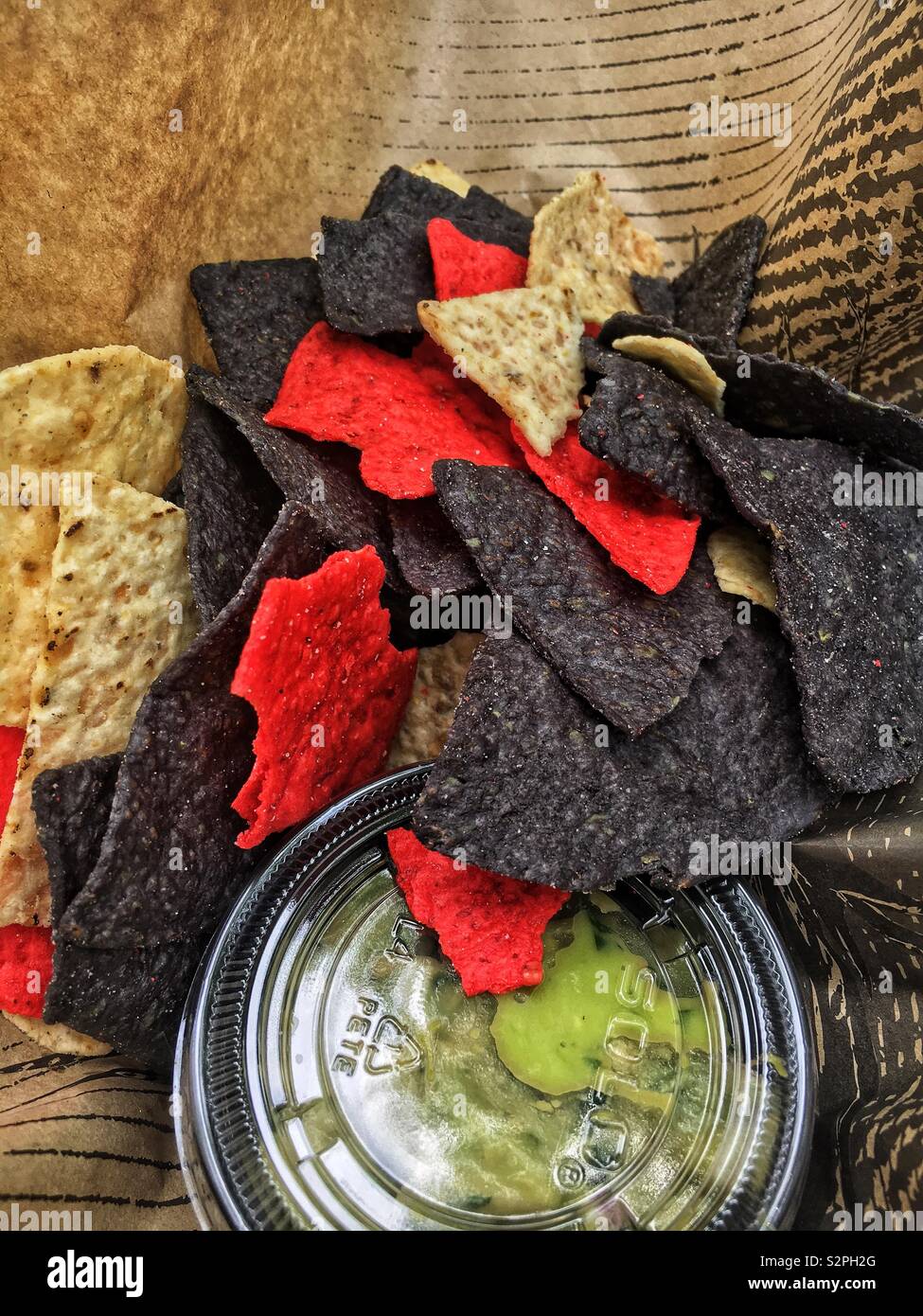 Variety of red, blue, and white corn chips set alongside a small tub of fresh green guacamole. - Smartphone Captured Stock Image Variety of red, blue, and white corn chips set alongside a small tub of fresh green guacamole. - Smartphone Captured Stock Image