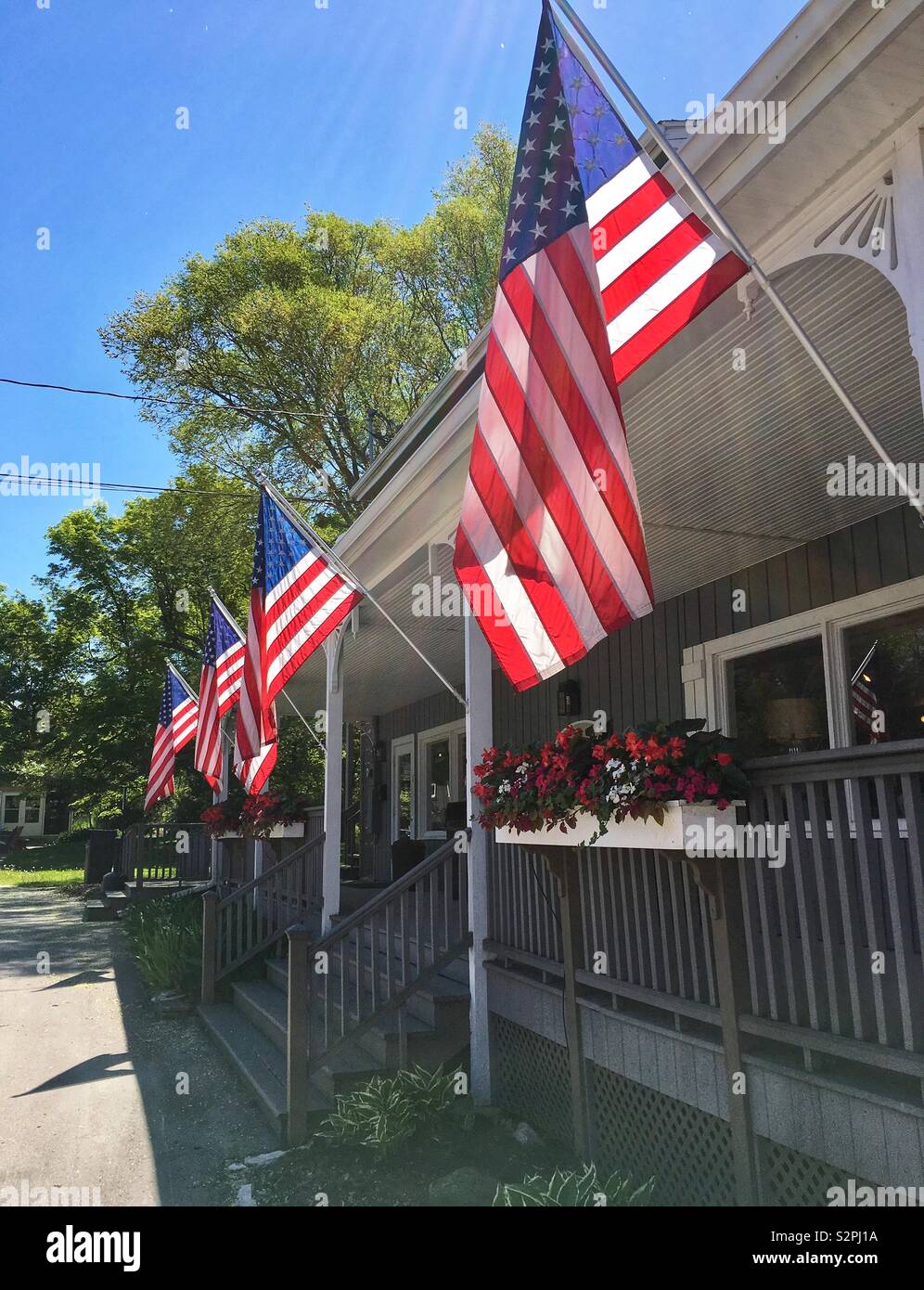 Multiple American flags fly patriotically on the front porch of a storefront on sunny summer day with blue skies in Egg Harbor WI - Smartphone Captured Stock Image