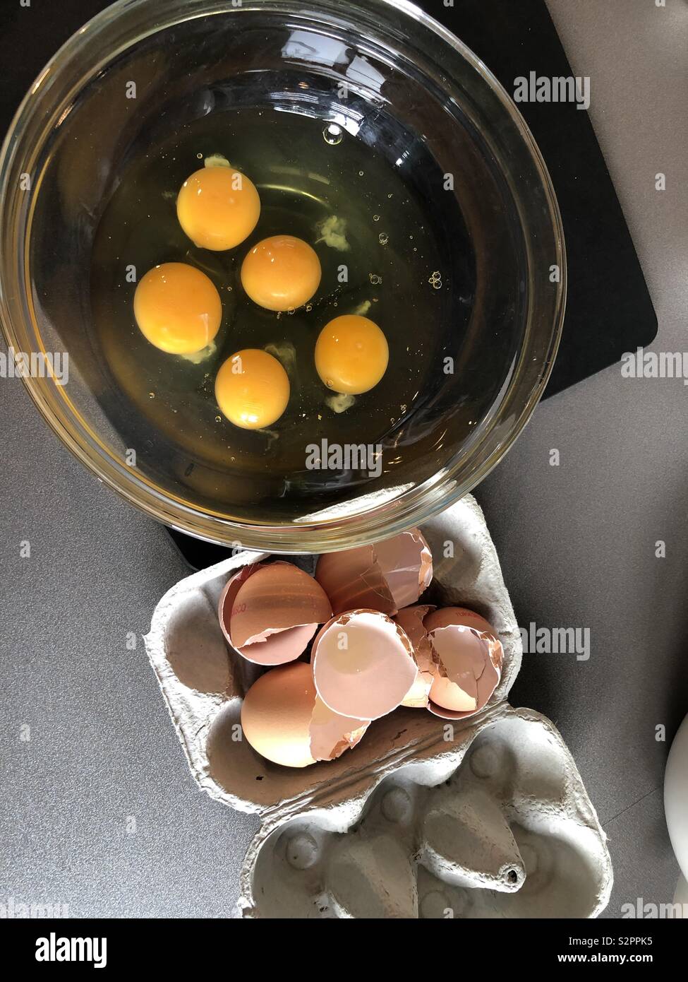 Five eggs broken into a bowl with shells in an eggbox - Smartphone Captured Stock Image