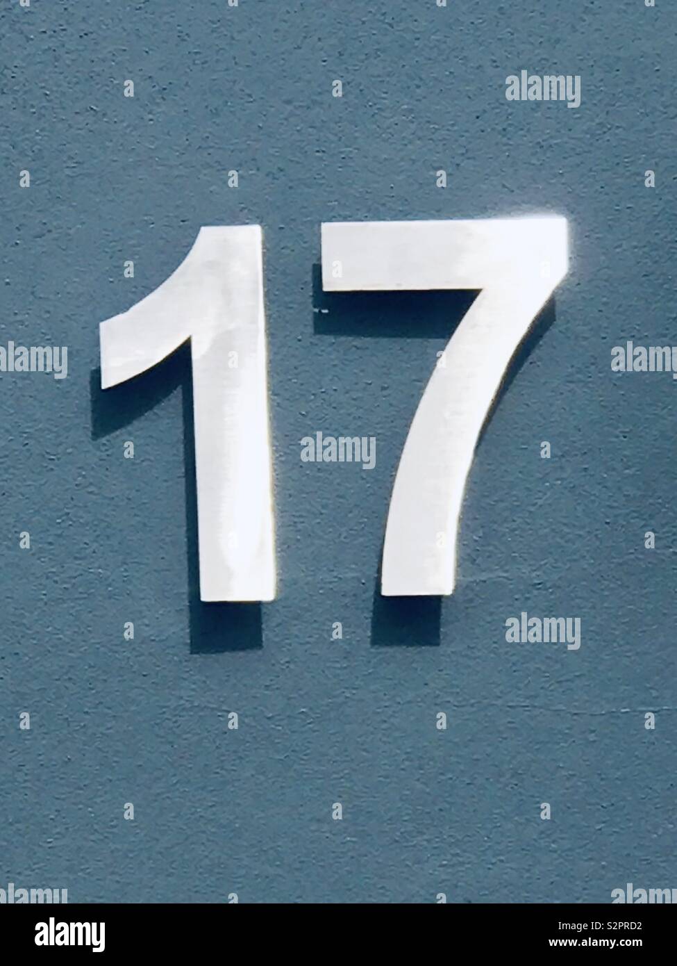 Number seventeen made of white painted metal on a  blue door - Smartphone Captured Stock Image