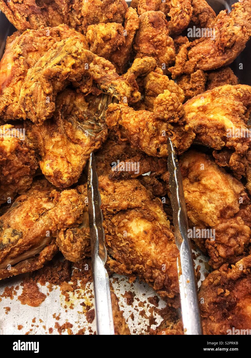 Fresh fried chicken in a banquet serving platter with tongs for scooping. - Smartphone Captured Stock Image