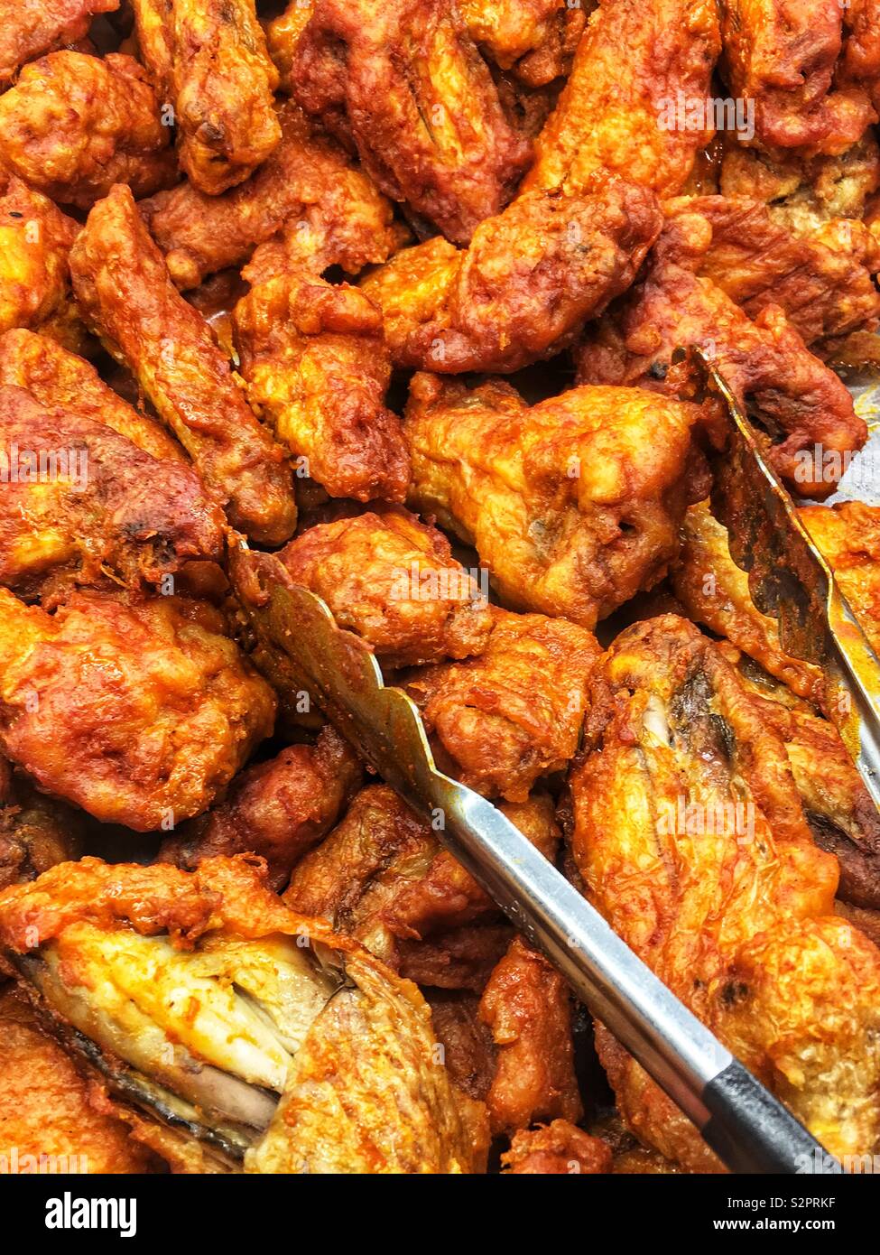 Fresh hot and spicy chicken wings in a buffet self service platter with  tongs for scooping Stock Photo - Alamy