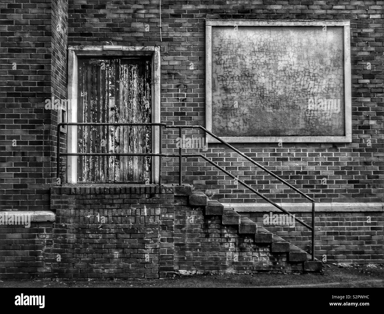 Old stairway to a locked door and blank poster on a derelic factory in Black and white - Smartphone Captured Stock Image