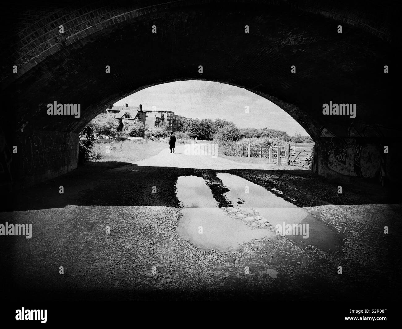 Image of a man who is seen in distance while walking away from an arch  under a railway bridge in east London - Smartphone Captured Stock Image