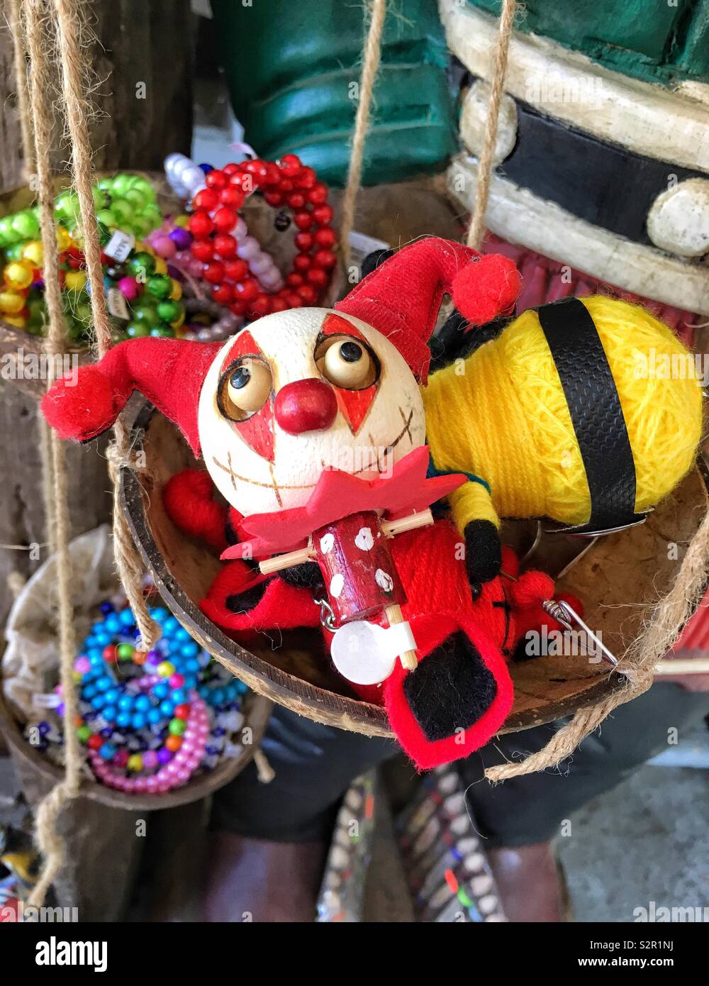Wooden pin jester doll next to a handmade Minion doll made of yellow yarn in a coconut surrounded by colorful beaded bracelets - Smartphone Captured Stock Image