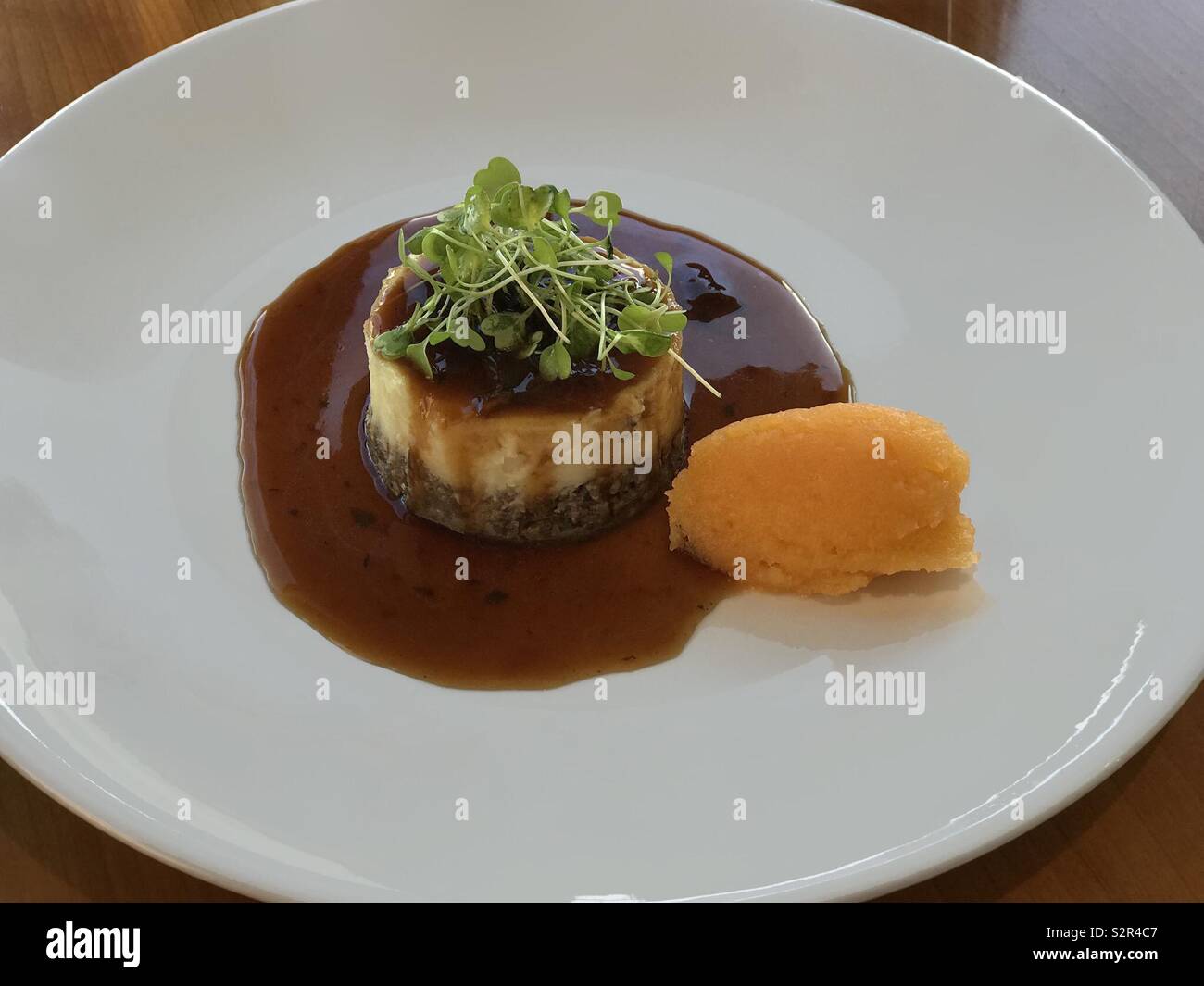 A traditional timbal of haggis and tatties (mashed potatoes), topped with watercress and with neeps (mashed rutabagas) on the side, is shown plated in a Scottish restaurant. Stock Photo