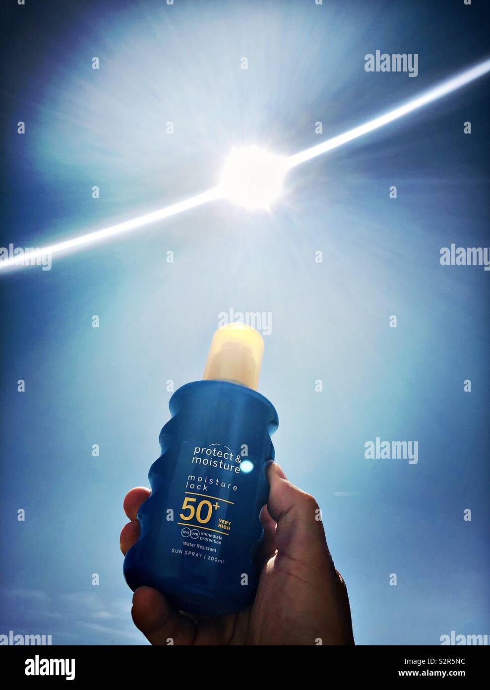 Sunscreen 50 factor sun cream held in hand  against the sunny sky Stock Photo