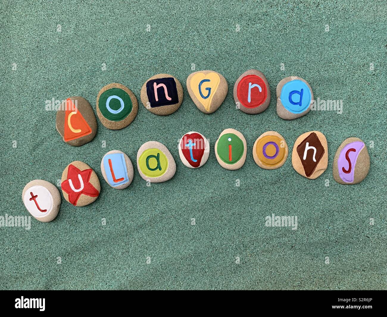 Congratulations text composed with multicolored painted pebbles over green sand Stock Photo
