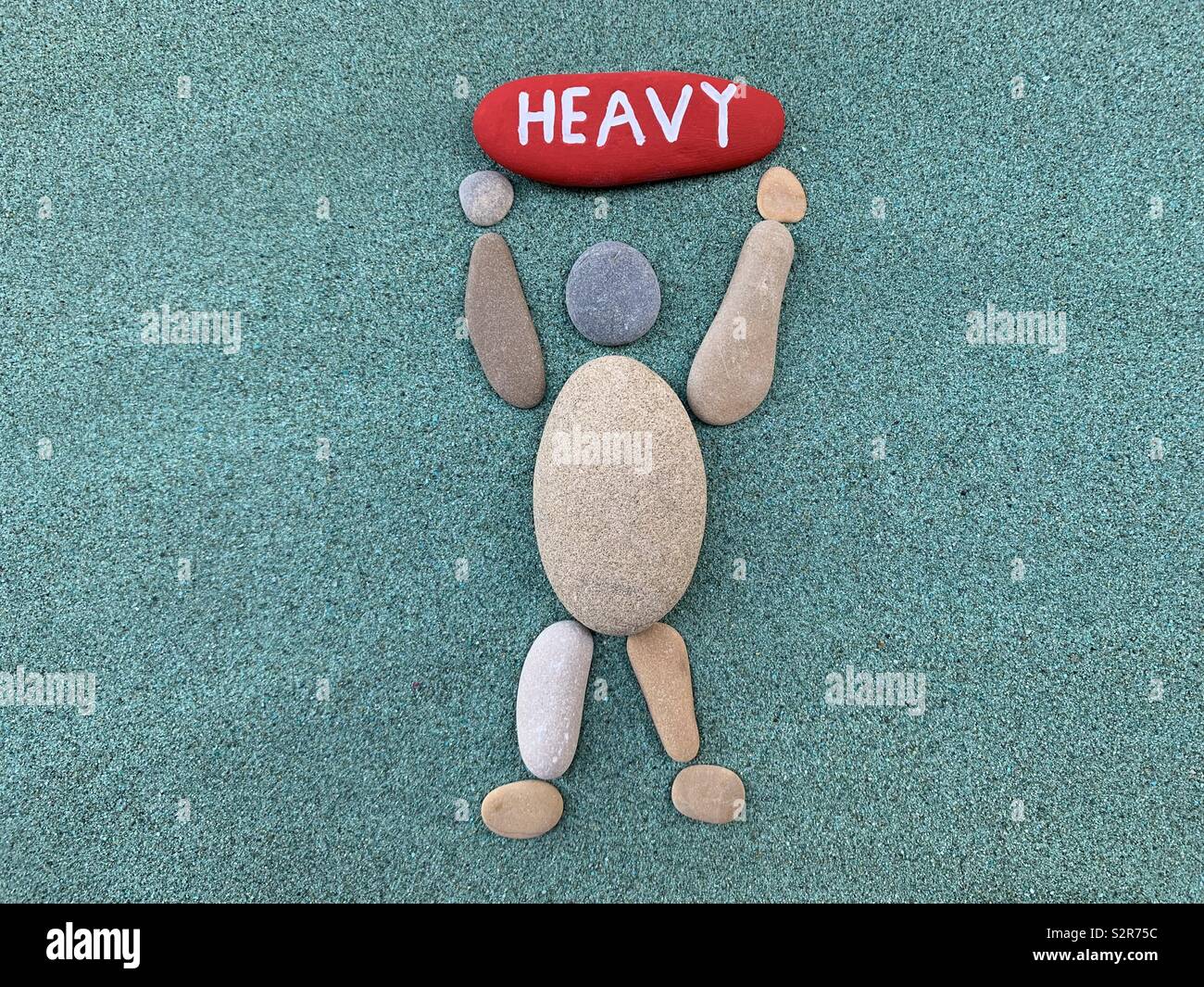 Heavy sign carved over a man composed with pebbles over green sand - Smartphone Captured Stock Image