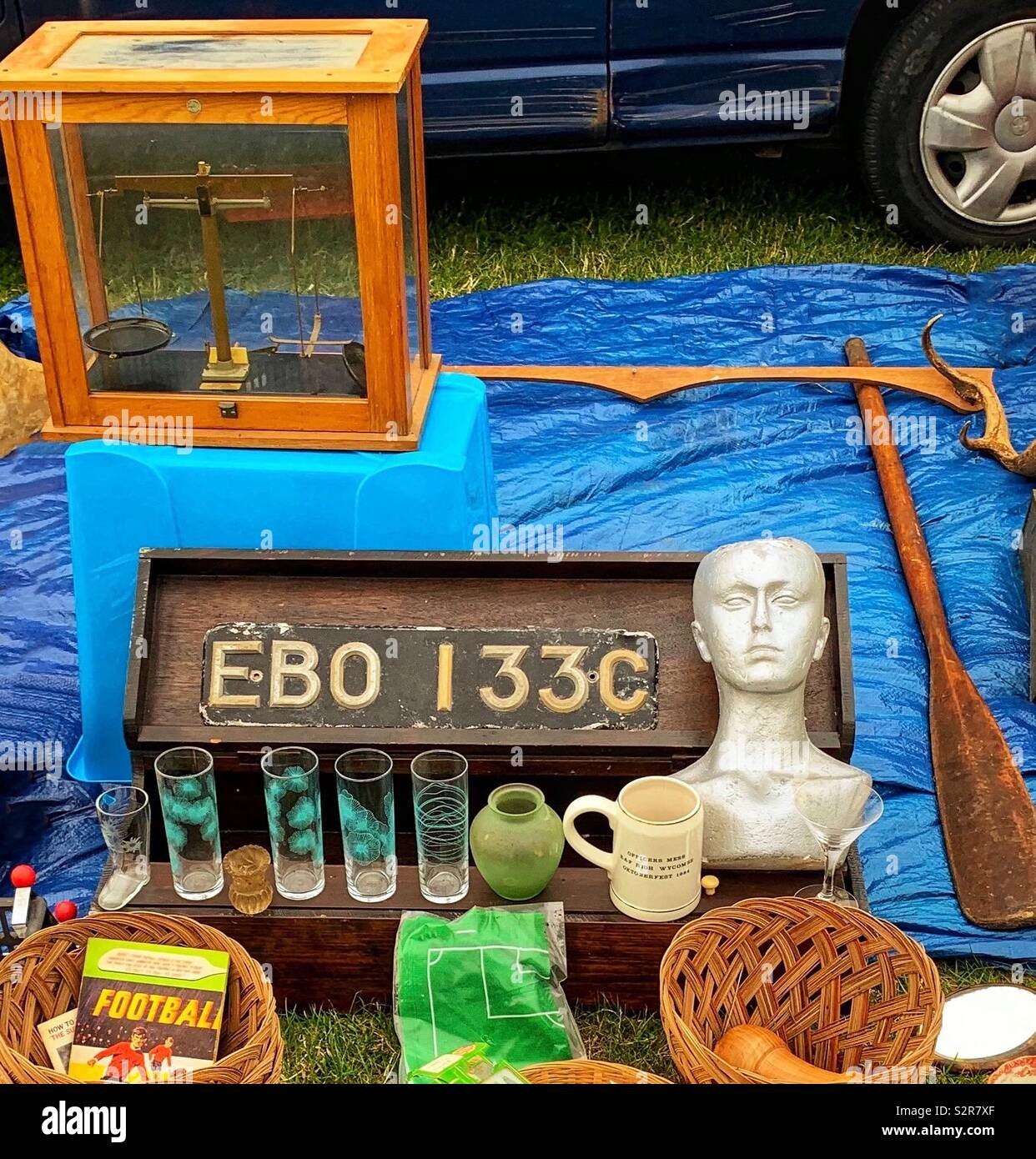Car boot sale items for sale laid out on tarpaulin with car behind