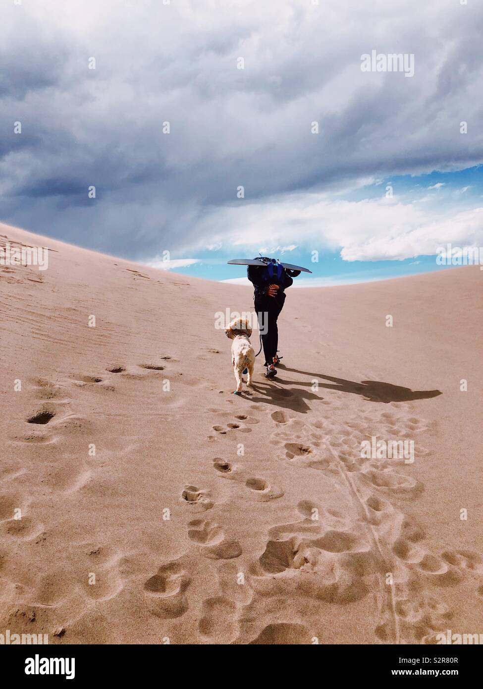 Woman and dog hiking up the sand dune at the Great Sand Dune National Monument in Colorado Stock Photo