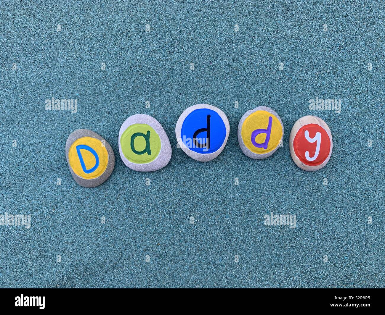 Daddy, Father’s day celebrated with a composition of creative colored pebble letters over green sand Stock Photo