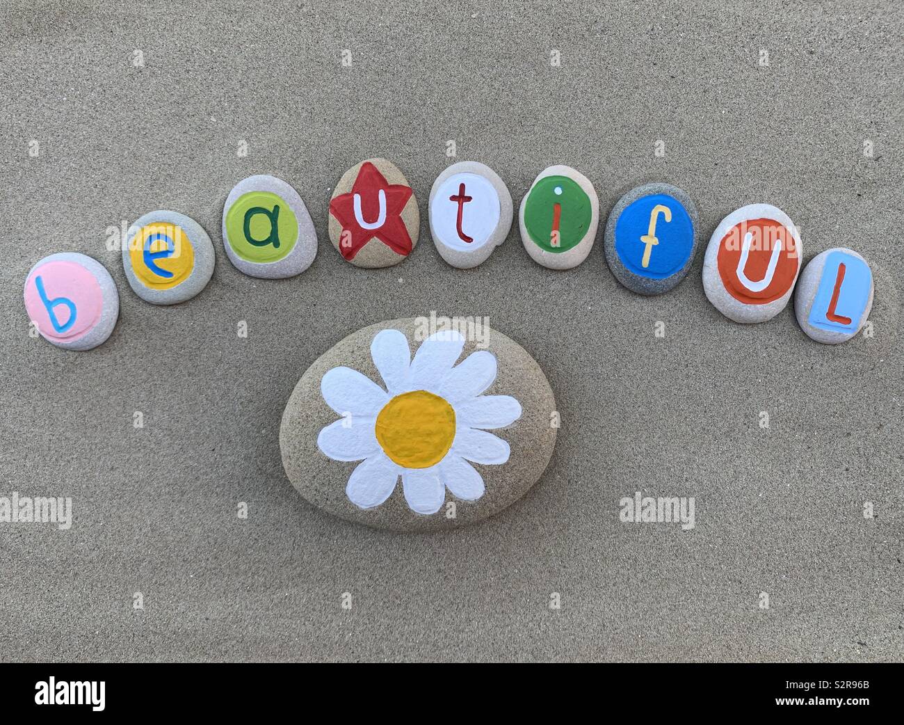 Beautiful text with painted stone letters and a stone daisy design over beach sand - Smartphone Captured Stock Image