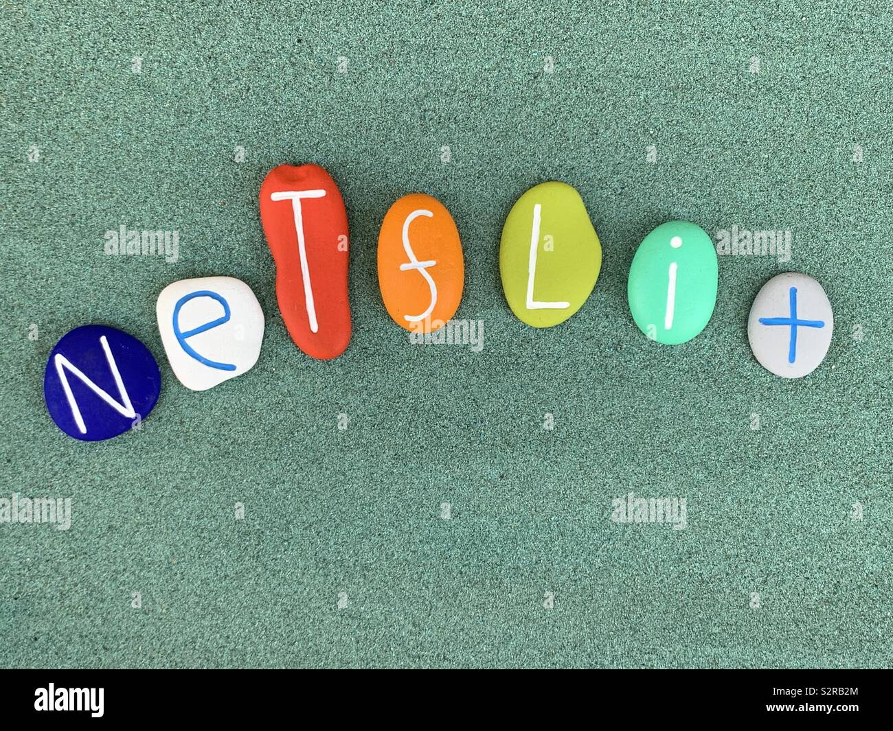 Netflix text composed with colored stone letters over green sand - Smartphone Captured Stock Image