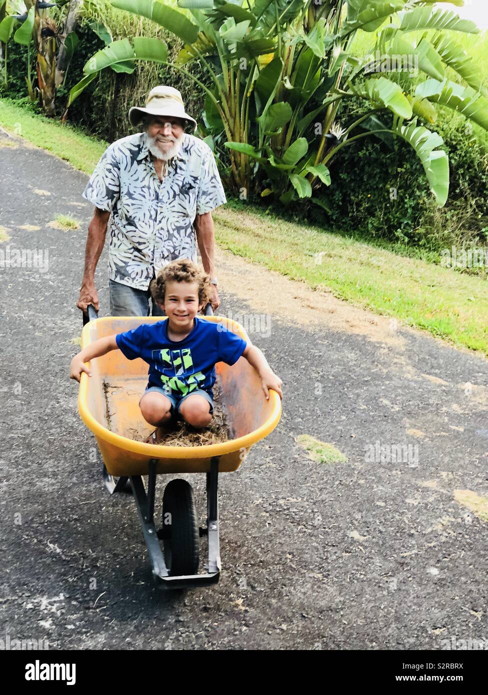 Grandfather pushing grandson in a wheelbarrow - Smartphone Captured Stock Image