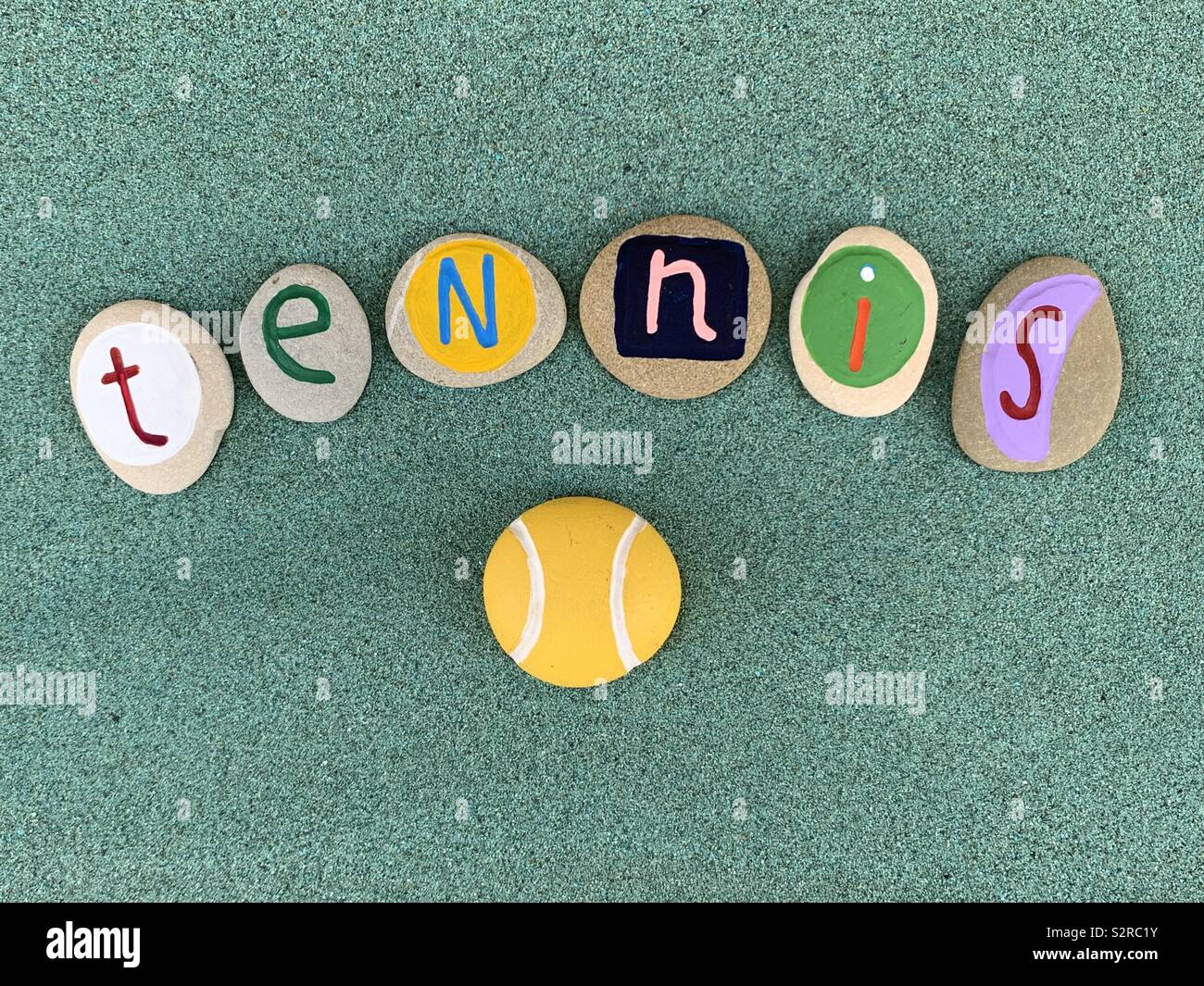 Tennis text composed with colored and carved stone letters over green sand - Smartphone Captured Stock Image
