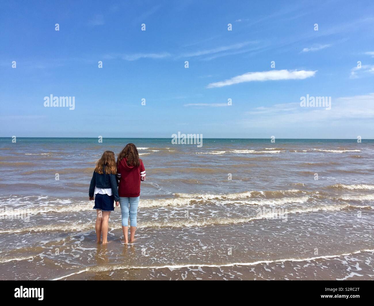 Looking out to sea, girls looking out to sea, paddling in the sea, sky, clouds, sea, sand, beach Stock Photo