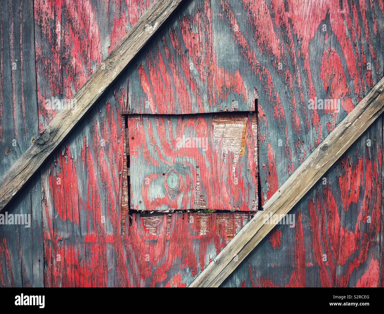 Square door in a faded red wooden hoarding. Stock Photo