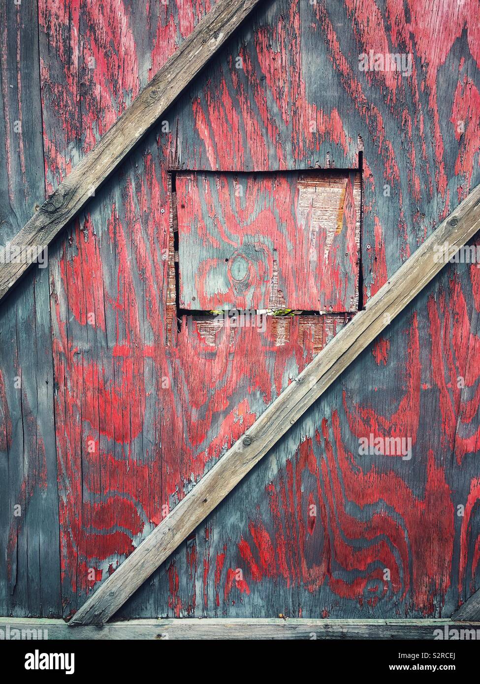 Faded red wooden hoarding with a square door cut into it. Stock Photo