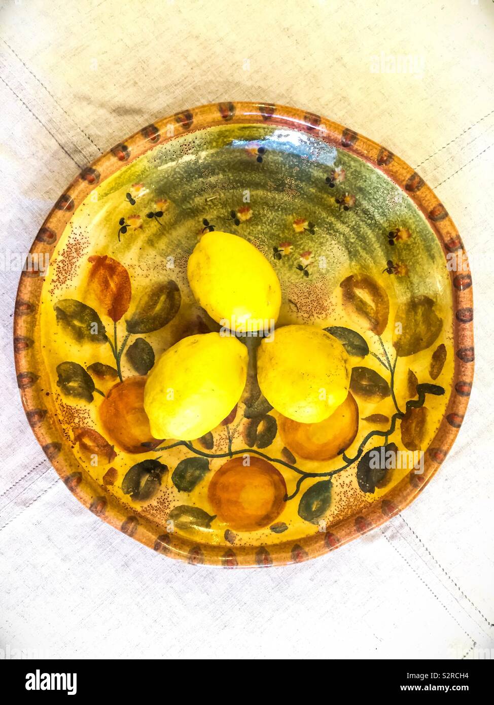 Three lemons on a colorful plate of Sorrento design from Ravello, the Amalfi Coast. The lemons are used for making the famous liqueur, Limoncello. Concepts: art, life, nature, Italian, floral, design Stock Photo