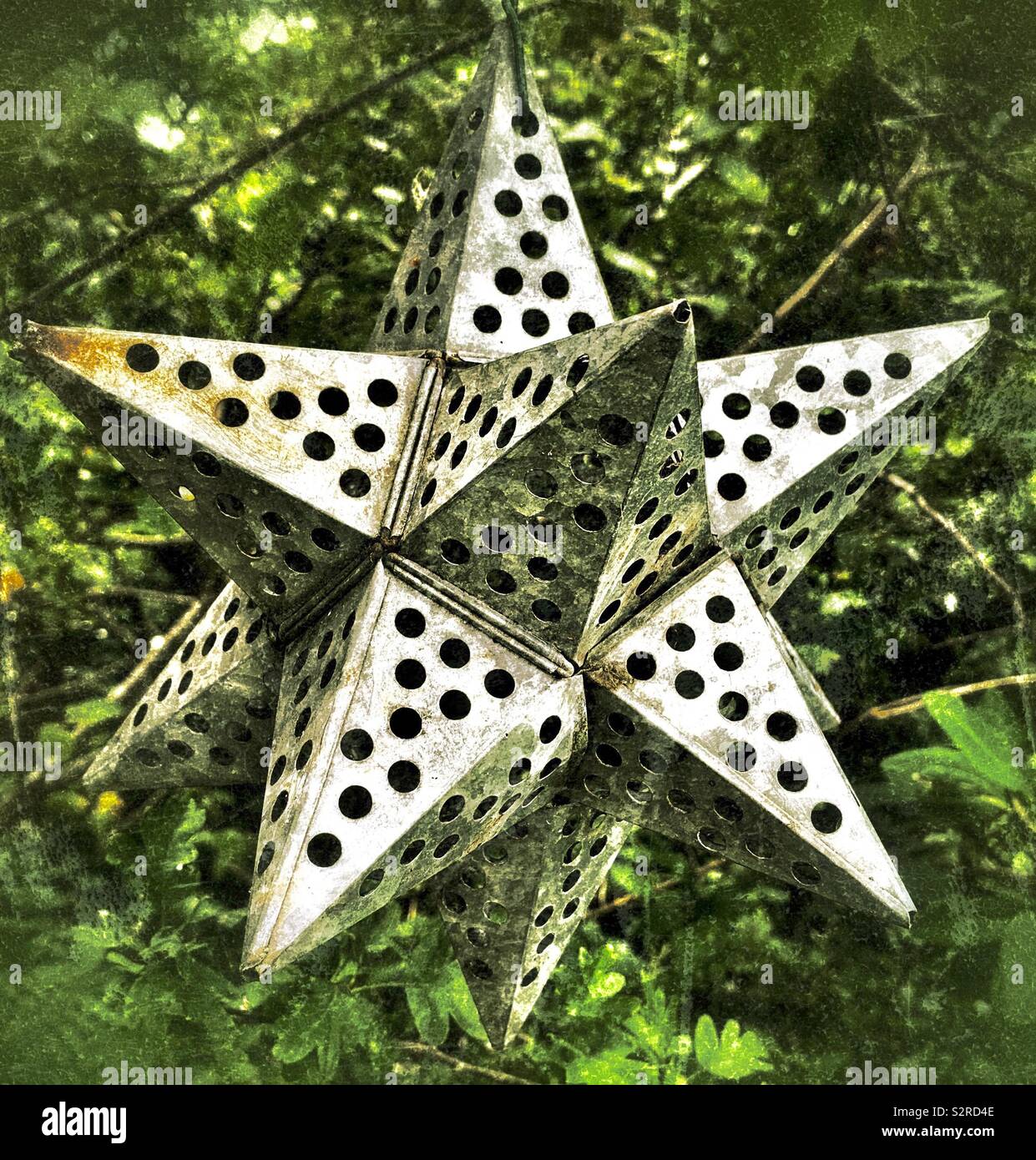 Geometric metal star shape garden ornament hanging from tree Stock Photo