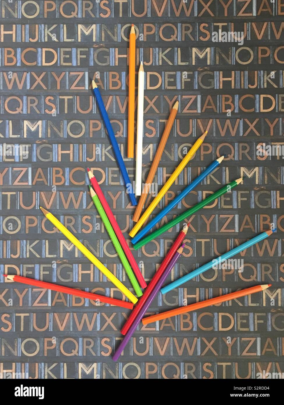 An assortment of brightly coloured pencils seen against an alphabetical chart - Smartphone Captured Stock Image