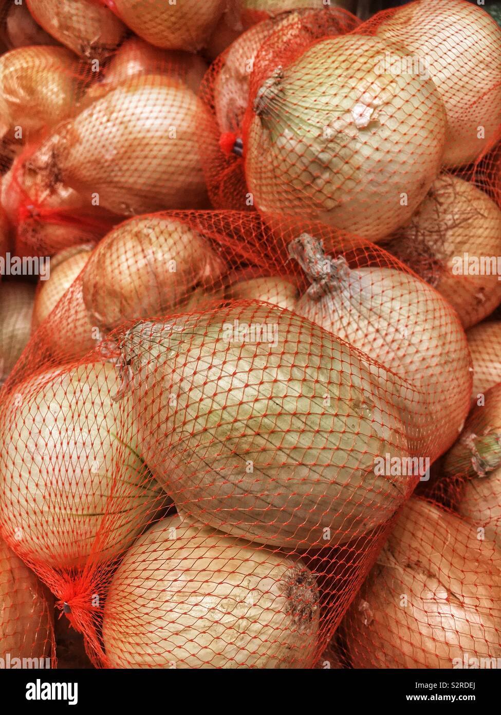 Fresh ripe yellow onions in red net bags. - Smartphone Captured Stock Image