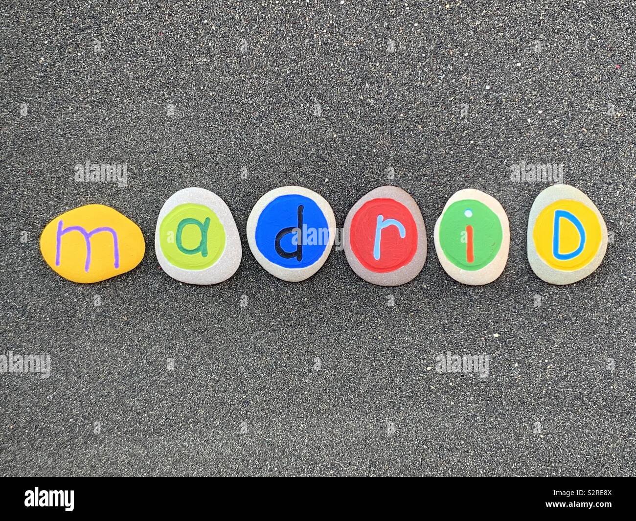Madrid, logo and souvenir design with colored pebble letters over black volcanic sand - Smartphone Captured Stock Image