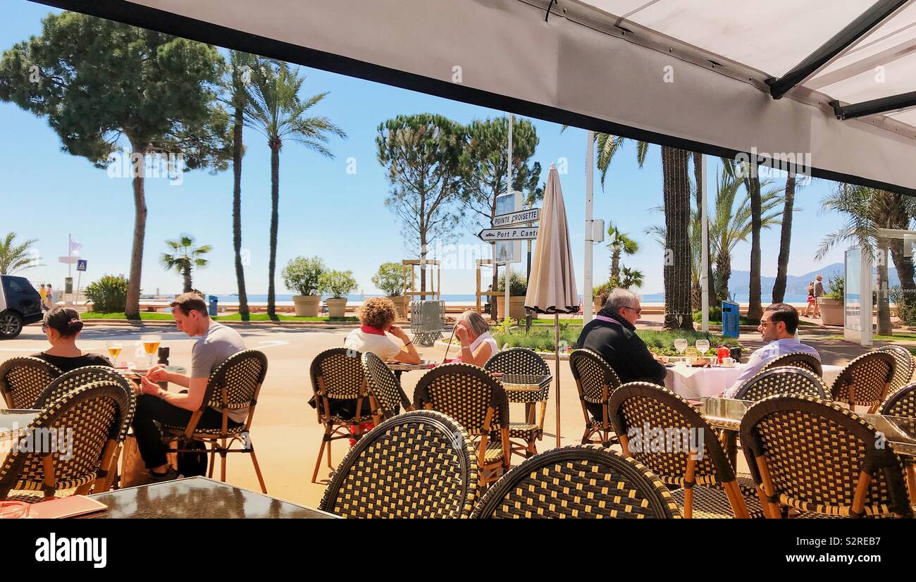 People sitting at tables in an outdoor cafe on the promenade in Cannes on the French Riviera - Smartphone Captured Stock Image