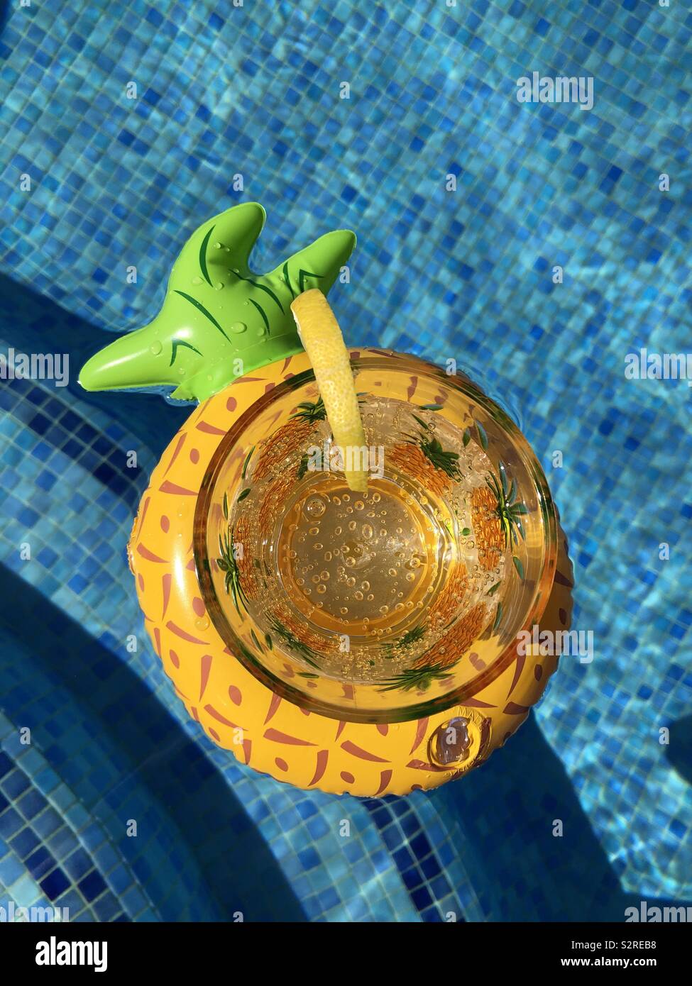 Glass of sparkling water and slice of lemon in an inflatable pineapple drink holder floating in a swimming pool, top view with copy space - Smartphone Captured Stock Image