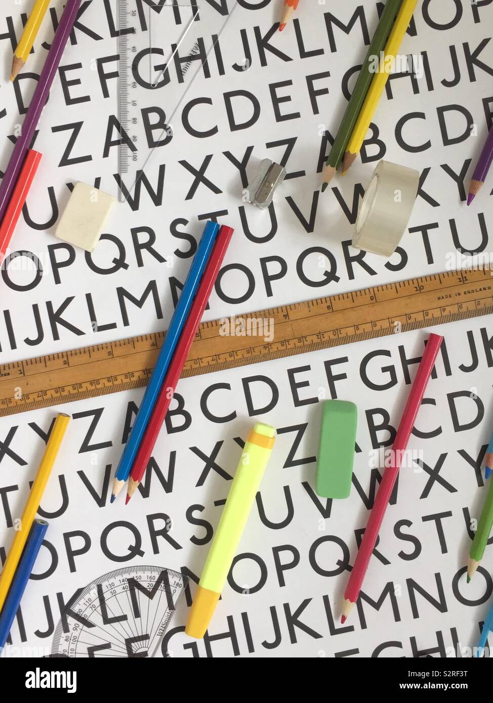 An alphabet table with an assortment of coloured pencils, eraser and vintage ruler Stock Photo