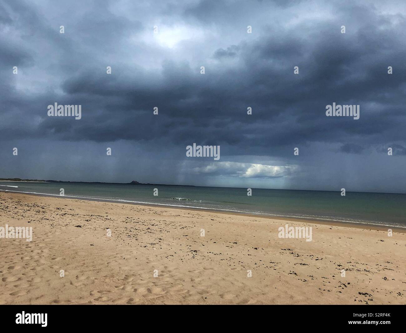 Rain showers over the sea at Ross Back Sands Northumberland with Lindisfarne in the distance - Smartphone Captured Stock Image