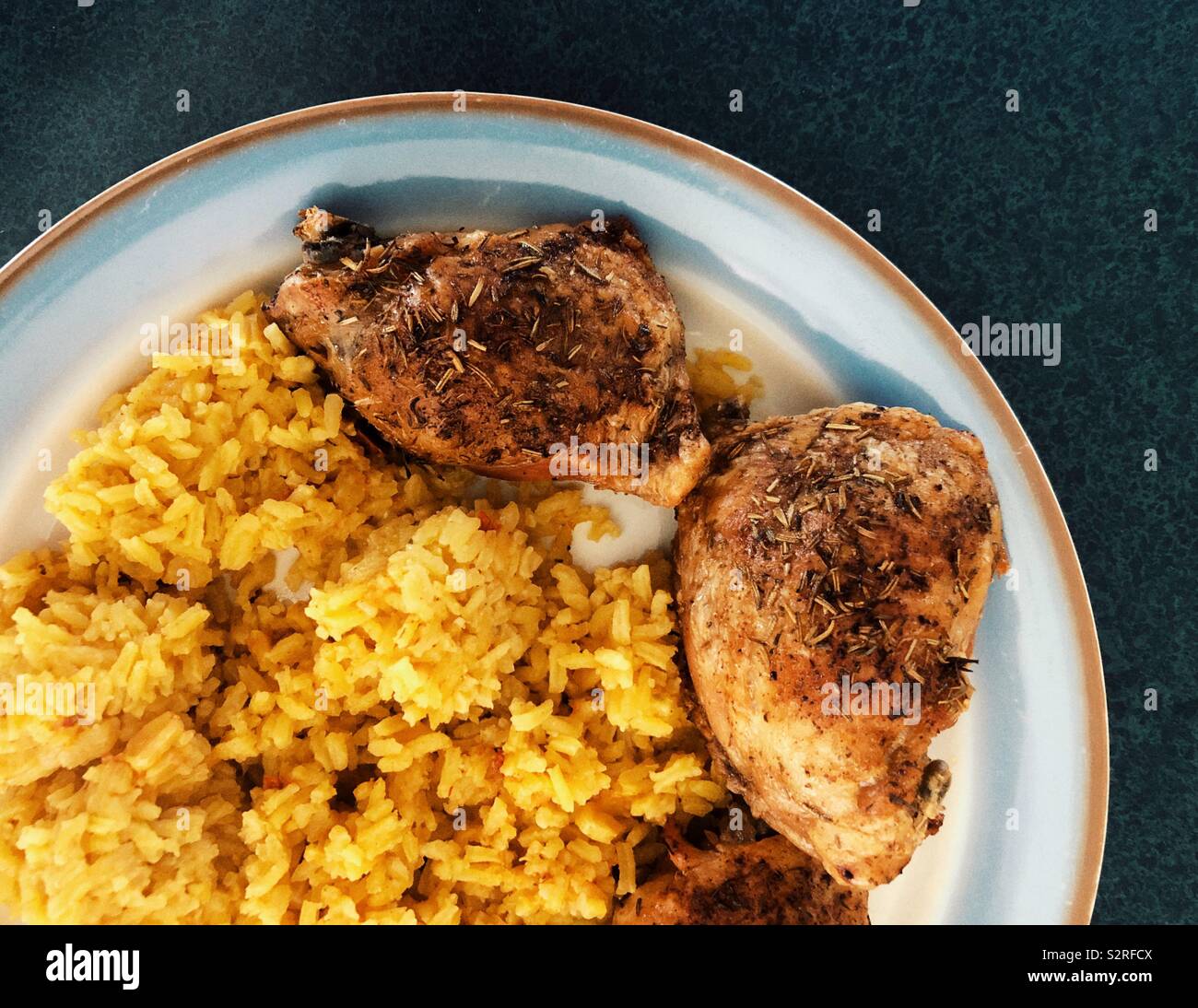 Flat lay partial plate view of baked herb crusted chicken thighs and yellow rice Stock Photo