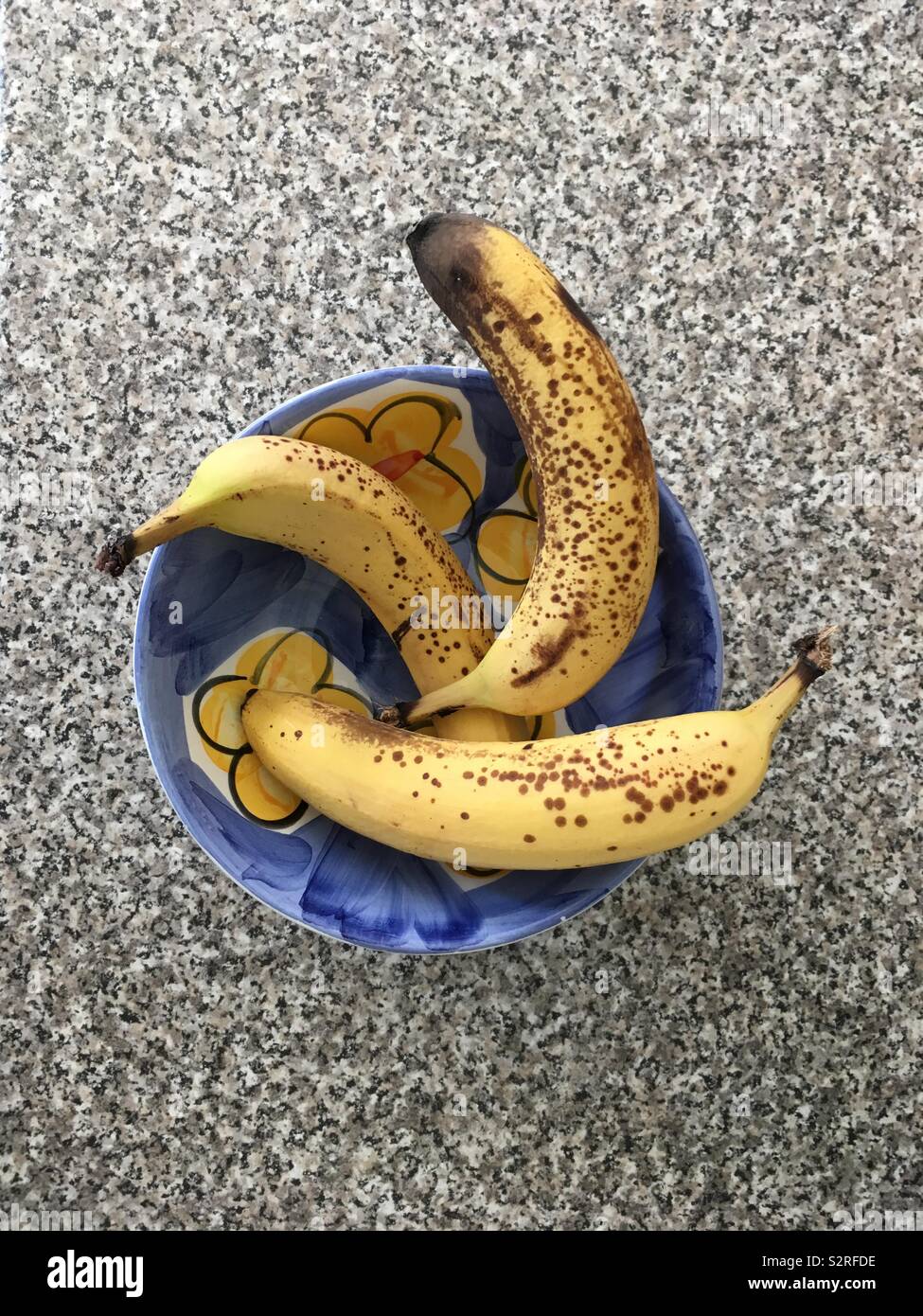 Three ripe bananas in a blue and yellow bowl on textured surface - Smartphone Captured Stock Image