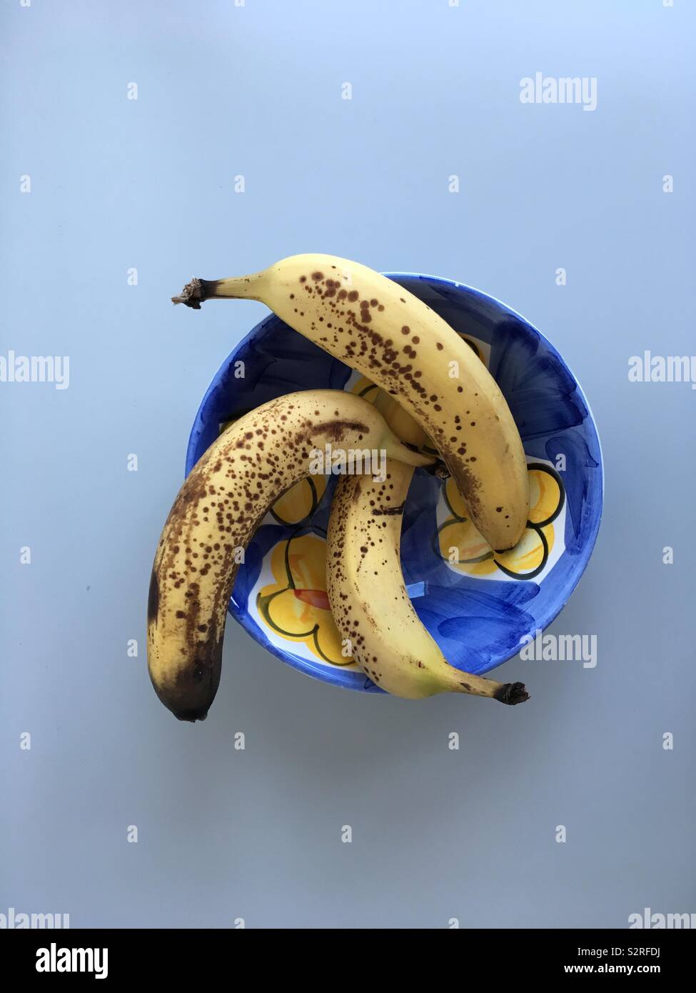 Three ripe bananas in a blue and yellow bowl on a light surface - Smartphone Captured Stock Image