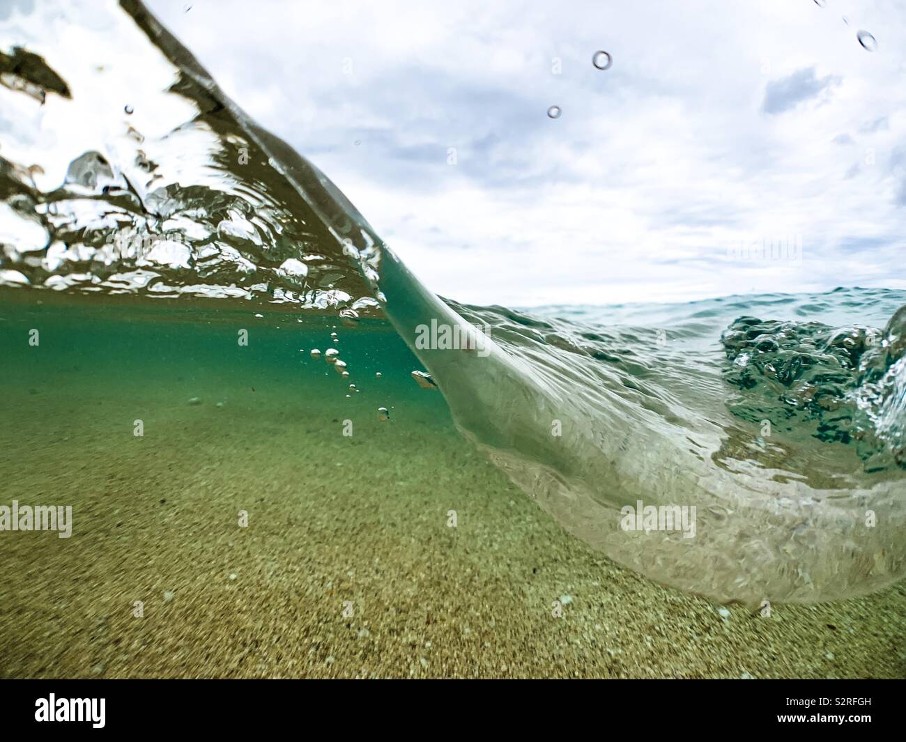 Over under photograph of ocean wave, sandy ocean floor and sky. Stock Photo
