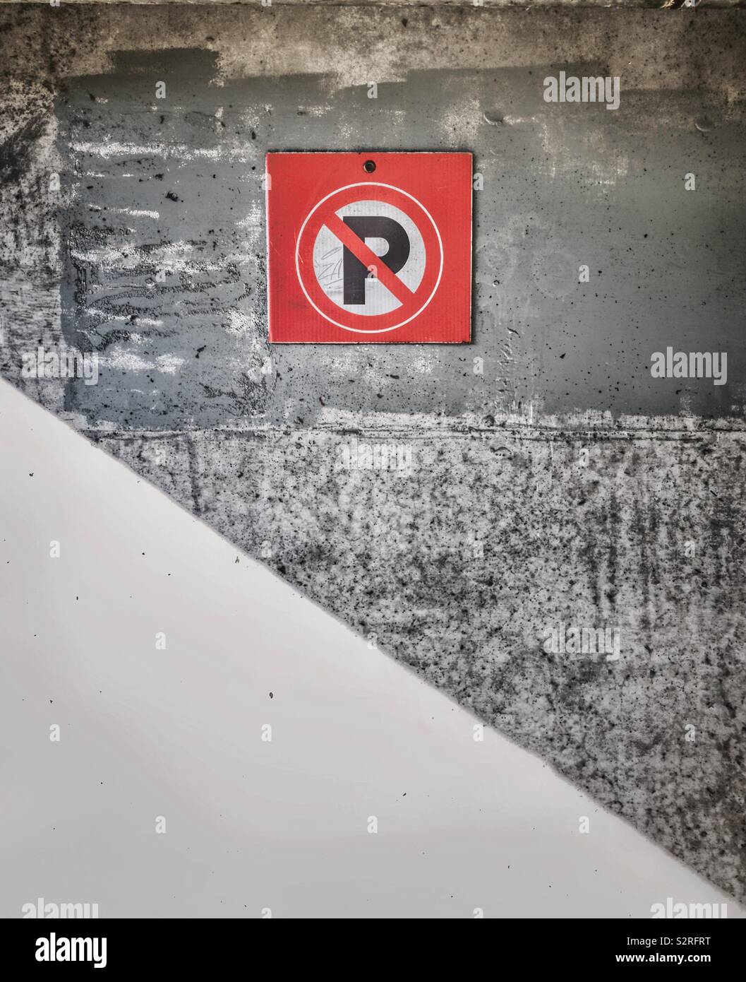 High contrast image of Bright red No Parking symbol on rough cement outdoor wall of parking garage. - Smartphone Captured Stock Image