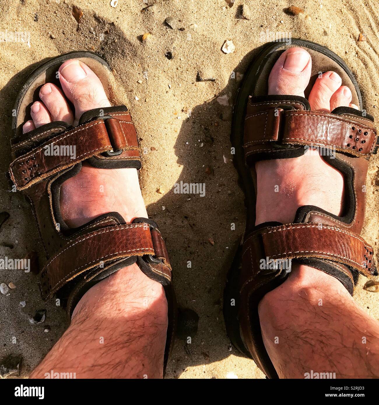 Sunburnt feet wearing sandals on a sandy beach. Stock Photo