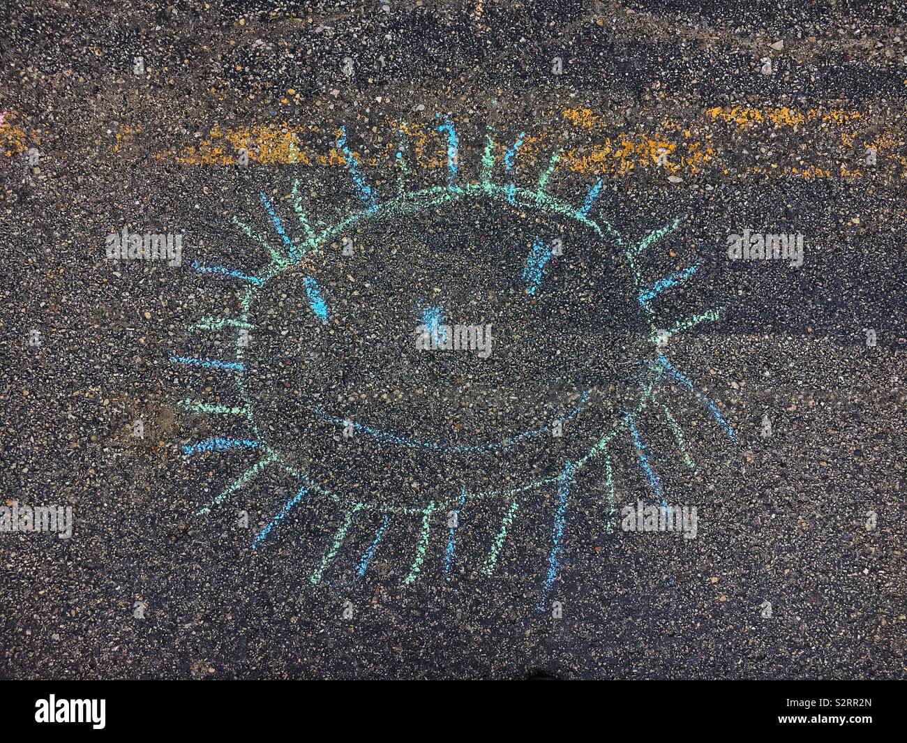 Chalk drawing on pavement of a smiling sun made by a third grader. Stock Photo