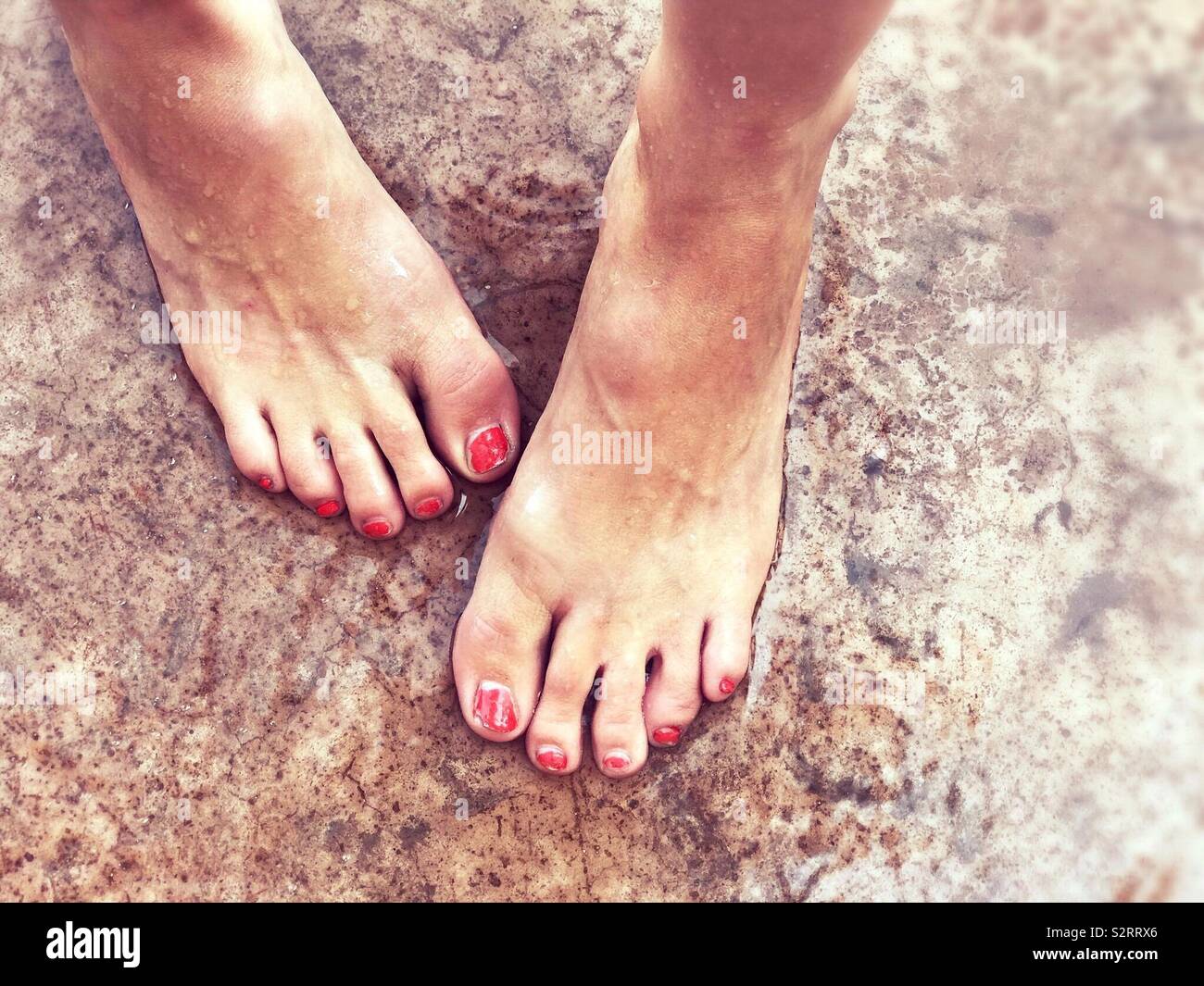 A woman’s bare feet standing on the wet ground outside on the concrete