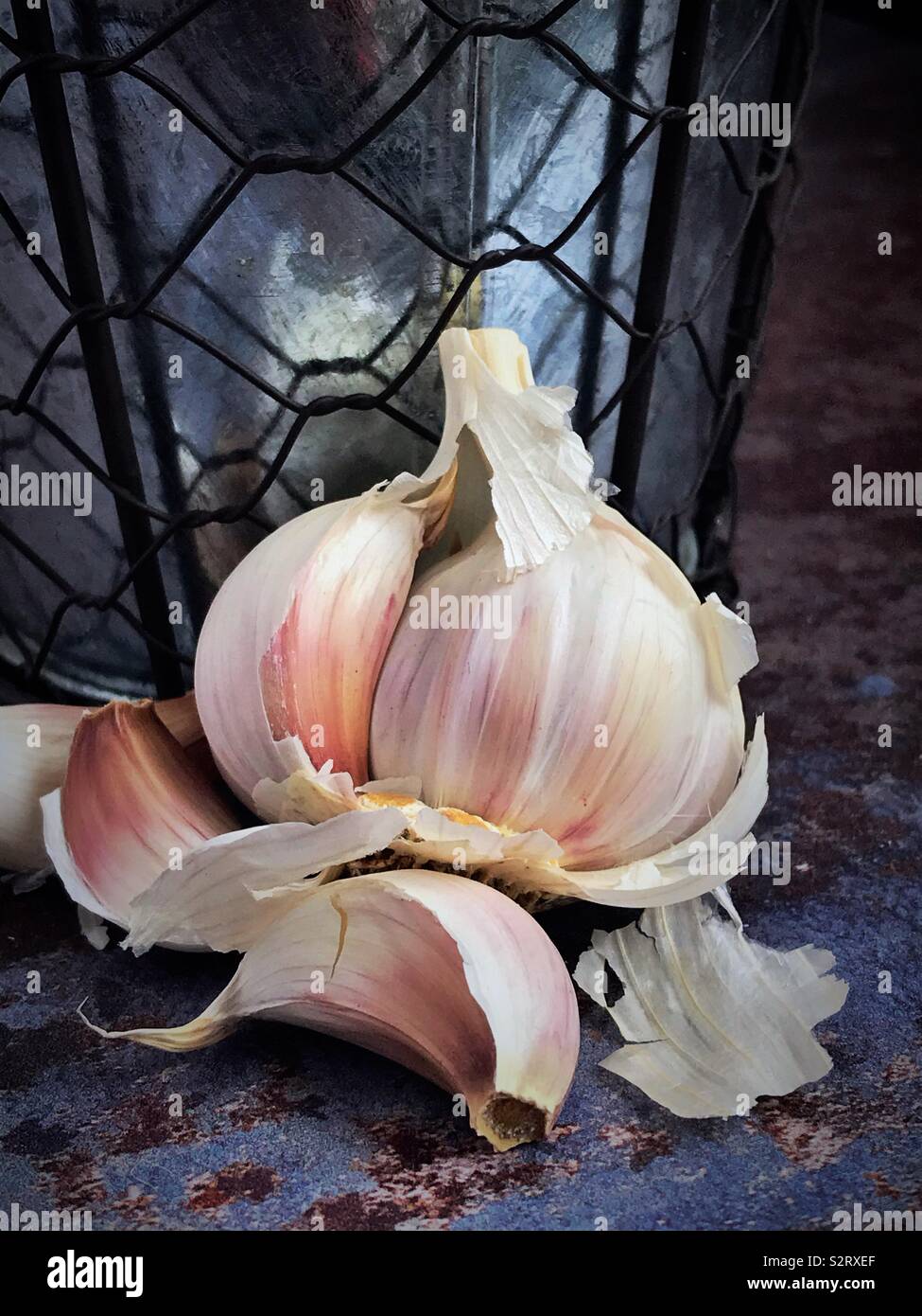 Garlic bulb broken open against a vintage metal pot. - Smartphone Captured Stock Image