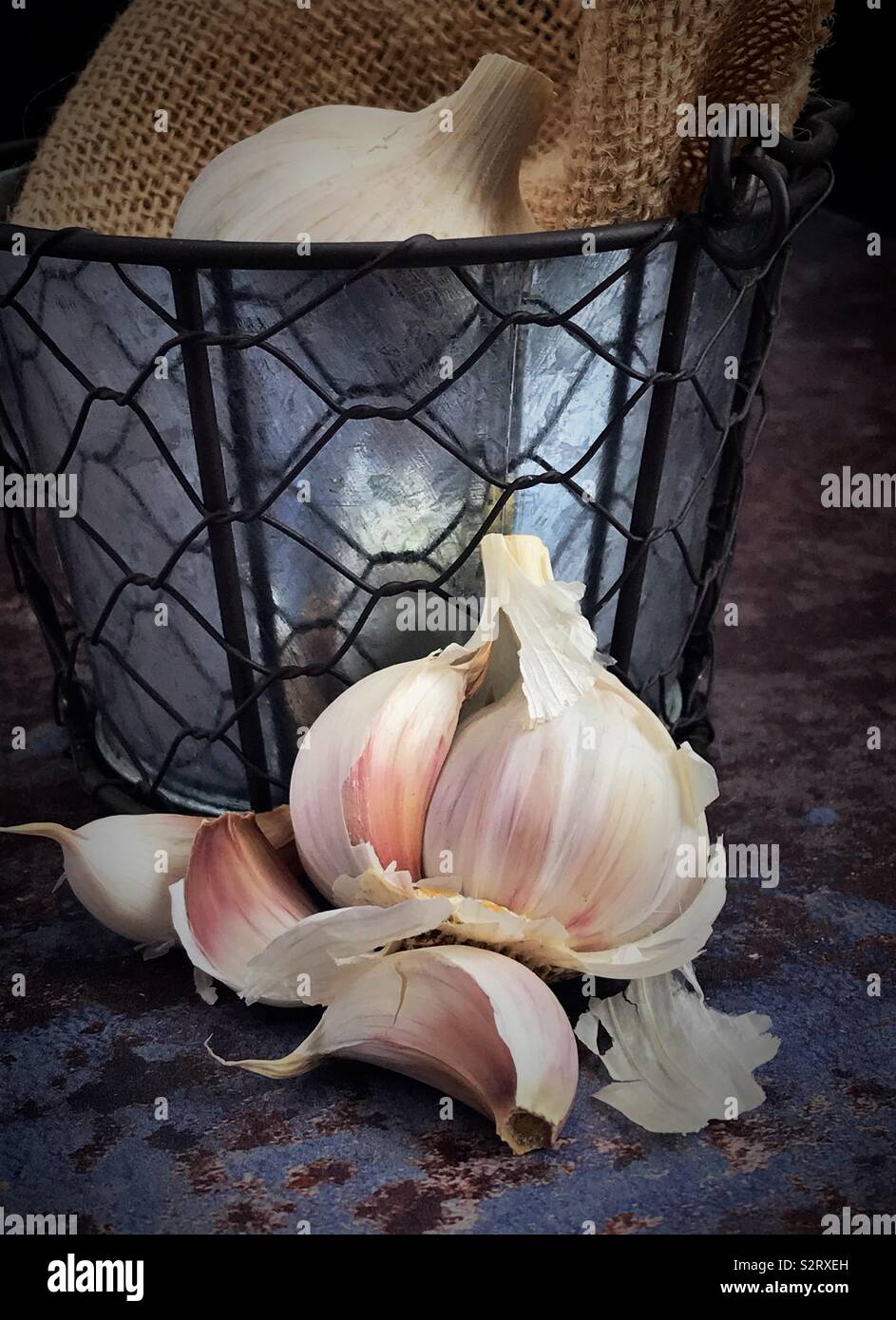 Garlic bulb broken open, next to a vintage metal pot containing garlic. - Smartphone Captured Stock Image